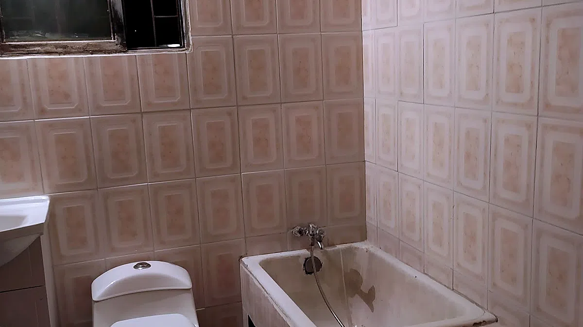 ANTES: baño antiguo con cerámica beige de relieve envejecida, tina esmaltada gastada, WC antiguo y una ventana en mal estado.