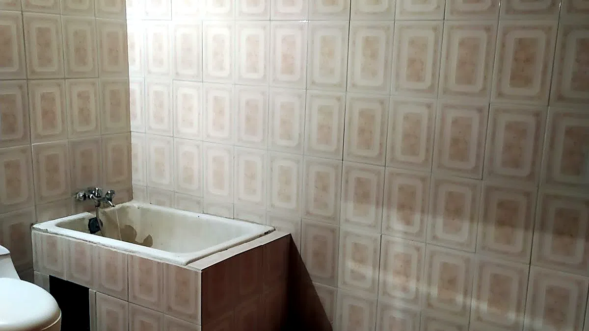 El mismo baño ANTES de remodelar: tina esmaltada antigua revestida con cerámica beige de relieve de la época y grifería vieja, el estado desde donde parte la obra.