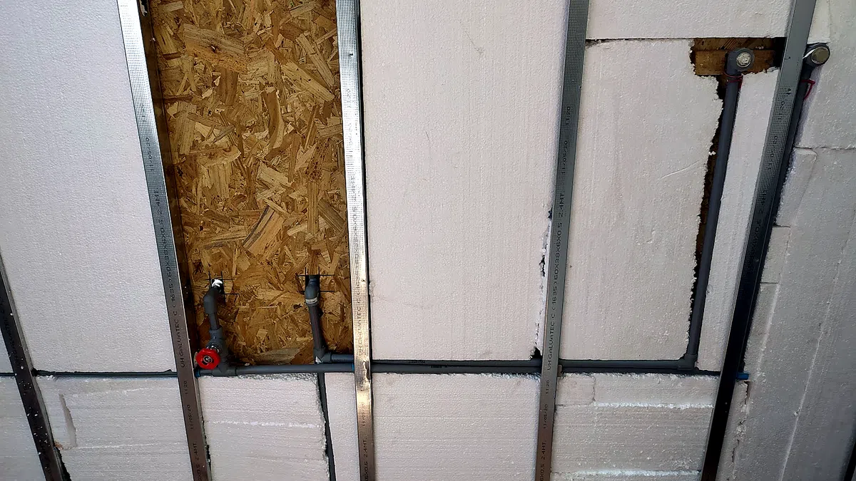 Instalaciones a la vista dentro de un tabique en obra: cañerías y ductos pasando entre la estructura metálica y la aislación, antes de cerrar el muro.