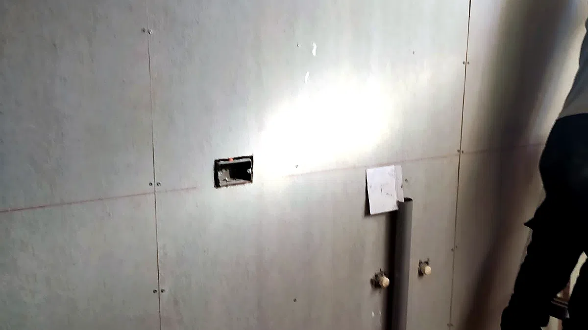 Muro interior revestido durante una remodelación, con una caja eléctrica embutida y la línea roja de un nivel láser marcada sobre la superficie.