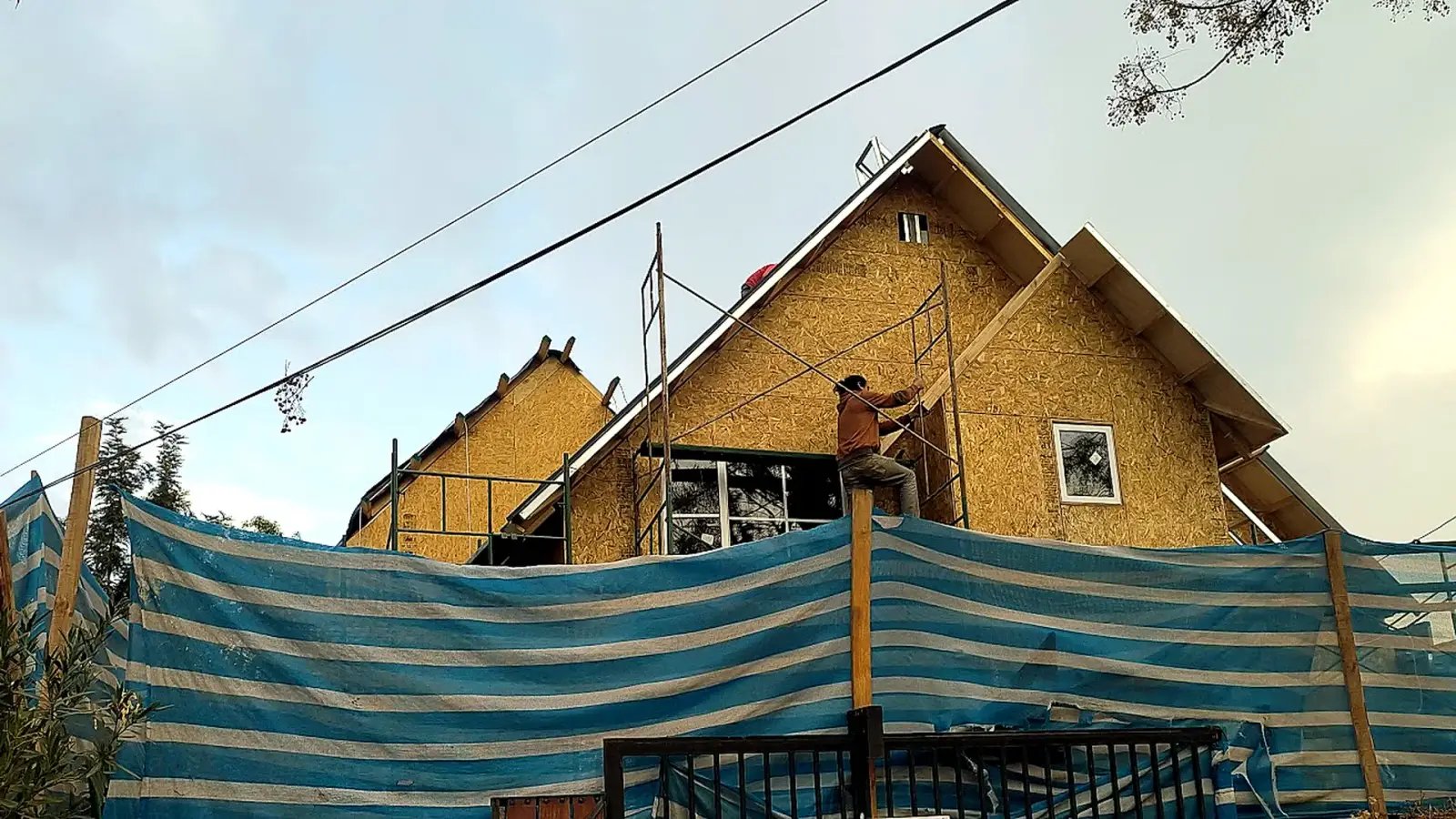Casa de dos pisos en construcción con techumbre montada y fachada revestida en OSB, con un trabajador en andamio