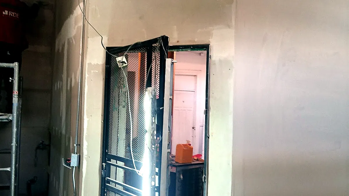 Interior de una vivienda en obra: muros estucados a medio terminar, un vano de puerta con marco metálico, conduit eléctrico a la vista y un andamio apoyado en un rincón.