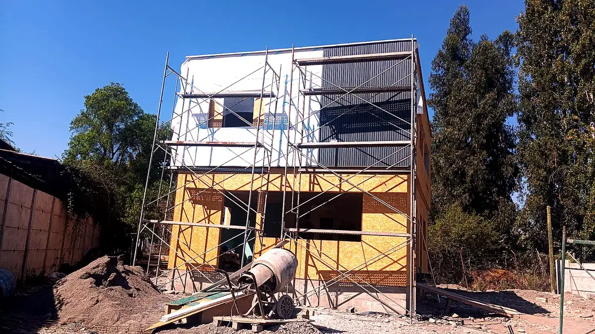 Casa de dos pisos en obra con la techumbre montada, andamios de trabajo y revestimiento de paneles OSB y plancha metálica.